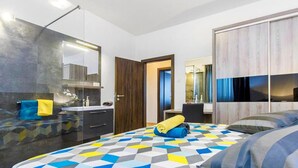 A modern hotel room with a geometric-patterned bedspread, a large mirror, a wooden door, and a view of the cityscape through the window.