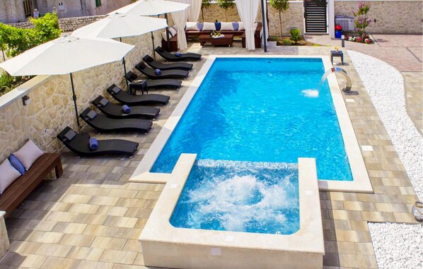 Una piscina rectangular con un jacuzzi en el centro, rodeada de tumbonas y sombrillas.