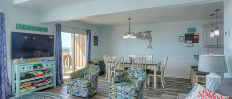 Una sala de estar con televisor, una mesa de comedor y dos sillones estampados.