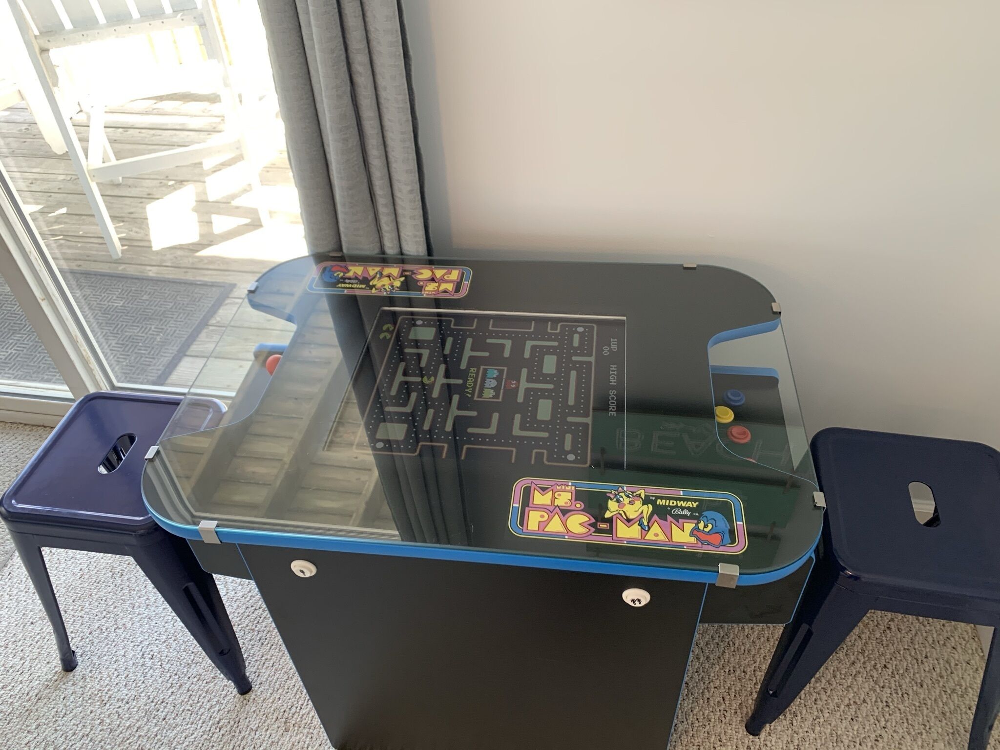 A Pac-Man arcade machine with a glass top and two stools.