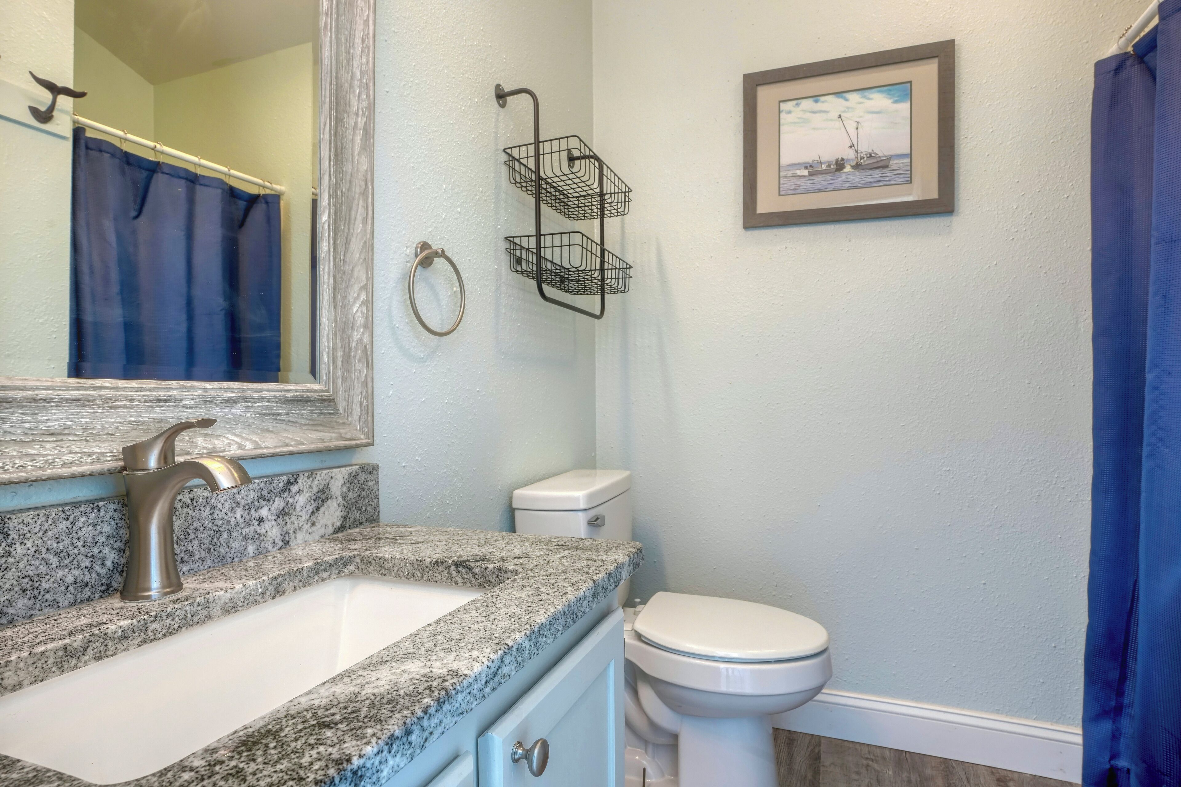 Une salle de bain avec un lavabo à vasque en granit, des toilettes blanches, un porte-serviettes, un tableau encadré au mur et un rideau de douche.