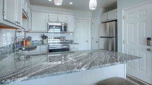 Una cocina moderna con armarios blancos, encimera de granito, electrodomésticos de acero inoxidable e iluminación colgante.