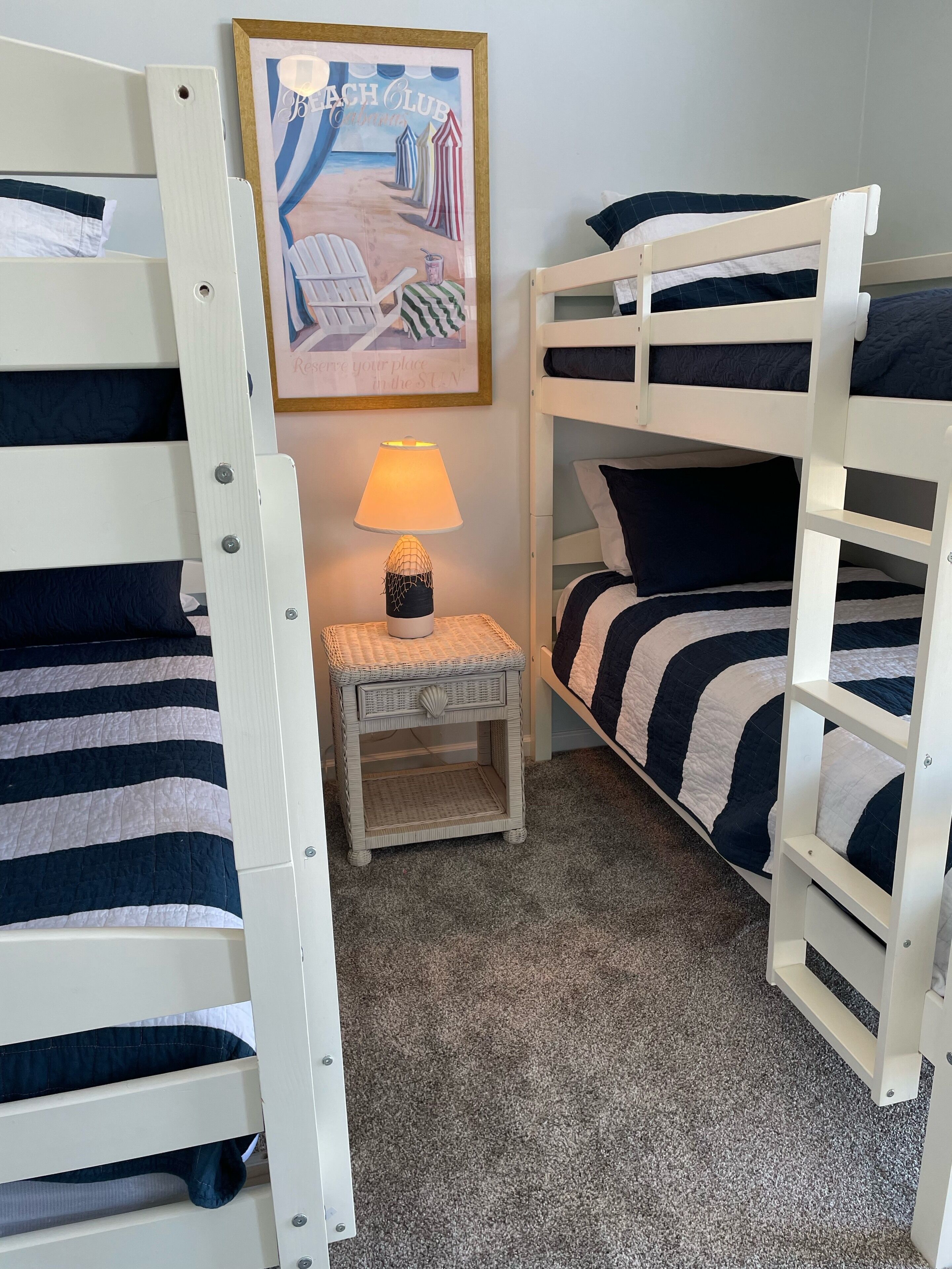 Een slaapkamer met stapelbed, een lijst met een foto van een strandclub, een tafeltje met een lamp en een gestreept beddegoed.