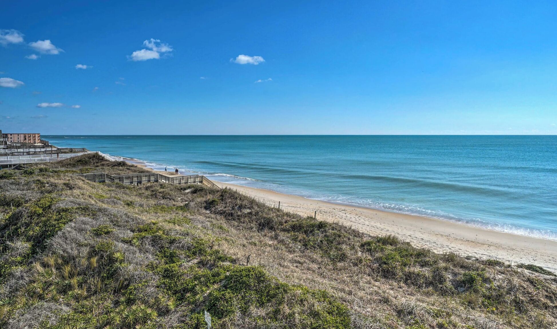 Une plage avec une promenade en bois menant à une étendue de sable, d’où l’on a une vue sur l’océan.