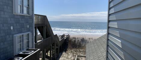 A view from a balcony overlooking a beach with a wooden deck and a house with a grey exterior.