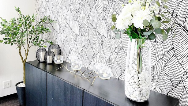 A modern interior with a black and white patterned wall, a dark wooden console table, and a vase with white flowers.