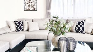 A living room with a beige sectional sofa, a glass coffee table, and a potted plant.