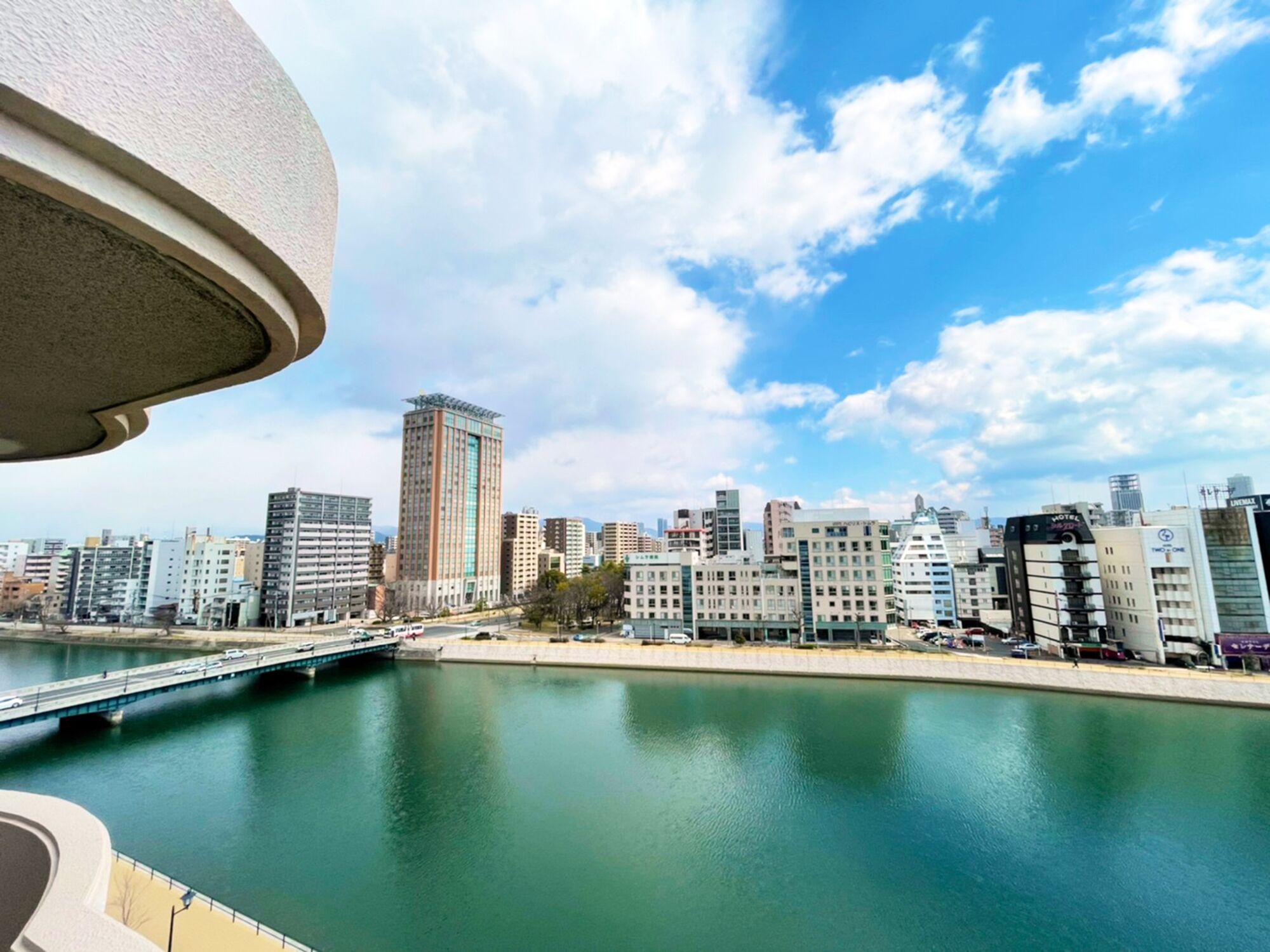 Un paisaje urbano con un río, un puente y diversos edificios, incluyendo un hotel alto.