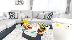 A modern living room with a grey sofa, a glass coffee table with food, and a white side table.