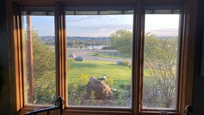 A room with a large window overlooking a grassy area with rocks and trees. - Farm Island Missouri River Views (Pierre)