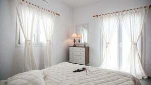 Une chambre à coucher avec un grand lit, une commode, un miroir et des rideaux légers.