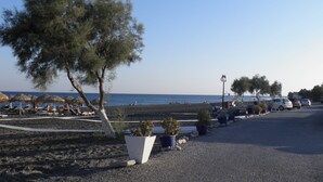 Un espace de stationnement situé au bord de la plage, agrémenté de plantes en pot, d’une rangée de parasols et offrant une vue sur la mer.