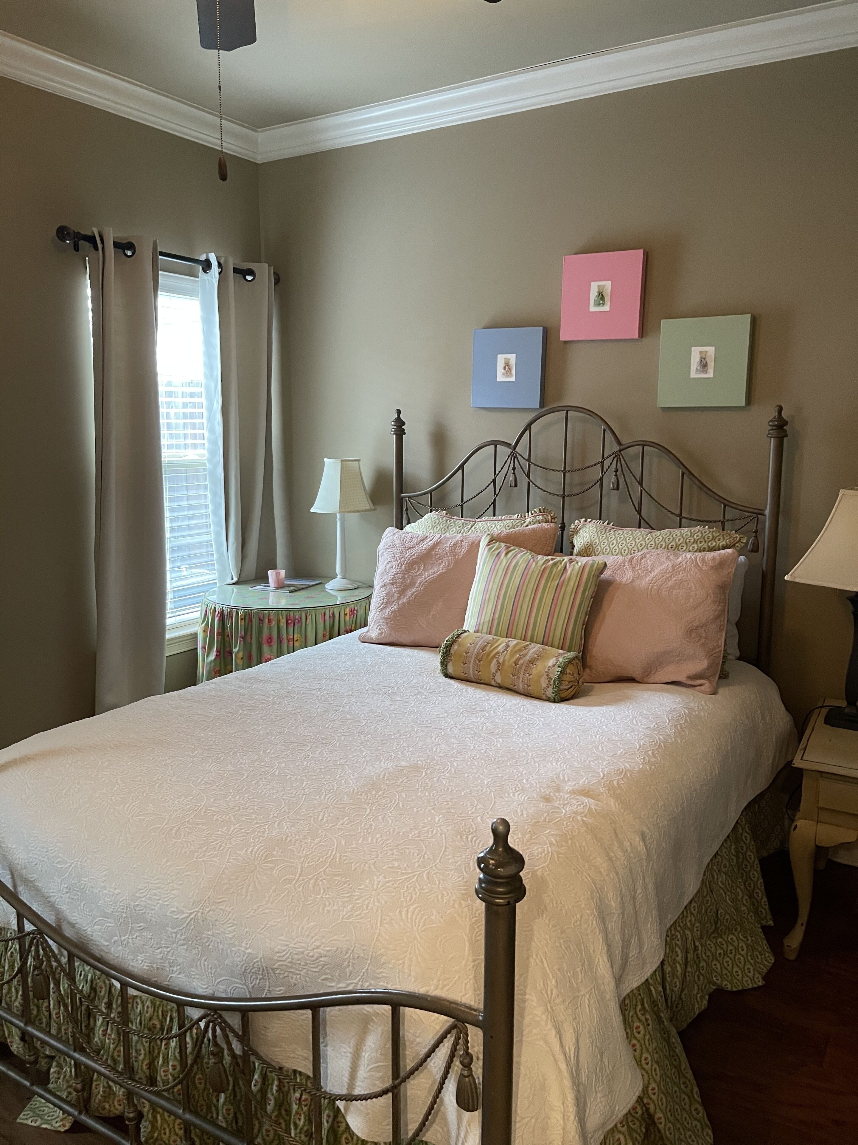 A neatly made bed with a metal frame, a bedside table with a lamp, and a window with curtains.