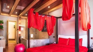 Une chambre à coucher avec un grand lit, des rideaux rouges, un ballon d’exercice rouge et une salle de bain moderne.