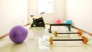 Une pièce équipée d’un vélo d’appartement, d’un ballon d’exercice violet et d’une barre d’haltères avec des poids.