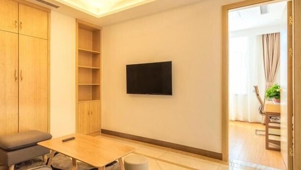 Une petite pièce moderne, avec un téléviseur fixé au mur, un meuble en bois, une petite table et un canapé gris.