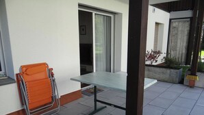 Terrassa amb taula i cadires, una porta corredissa de vidre i una petita zona de jardí.