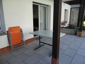 Eine Terrasse mit Tisch und Stühlen, eine Glastür und ein kleiner Gartenbereich.