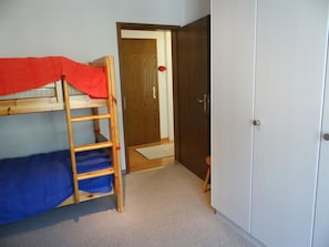 Une chambre avec un lit superposé, une armoire et une porte donnant sur une autre pièce.