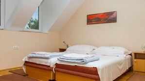 Un dormitorio con techo inclinado, cama con estructura de madera, mesita de noche, lámpara y un cuadro en la pared.