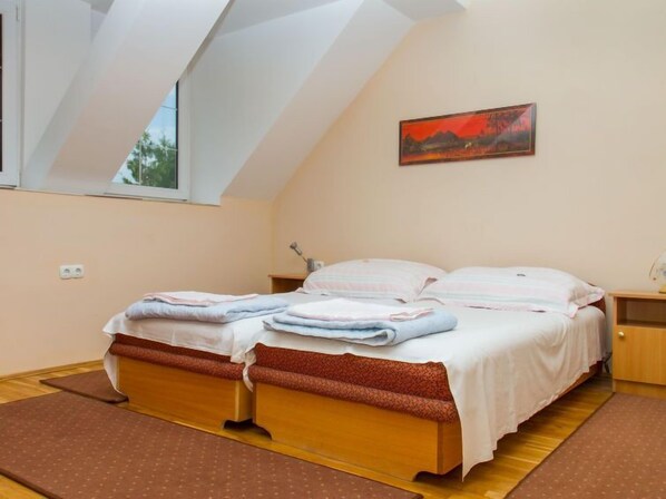 Una camera da letto con soffitto spiovente, un letto con struttura in legno, un comodino, una lampada e un quadro appeso al muro.