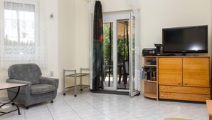 A living room with a sofa, a TV on a wooden cabinet, and a sliding glass door leading to a balcony. - Vacation home Leon by Interhome (Balatonmariafurdo)