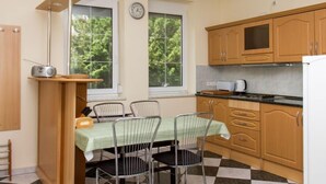 Una cocina compacta con armarios de madera, un microondas y un comedor con sillas de metal y un mantel verde.