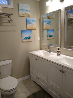 A bathroom with a white toilet, a sink with a mirror, and three beach-themed paintings on the wall.