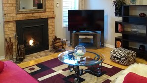 Ein Wohnzimmer mit Kamin aus Backsteinen, einem Flachbildfernseher, einem Glastisch und einem roten Sofa.