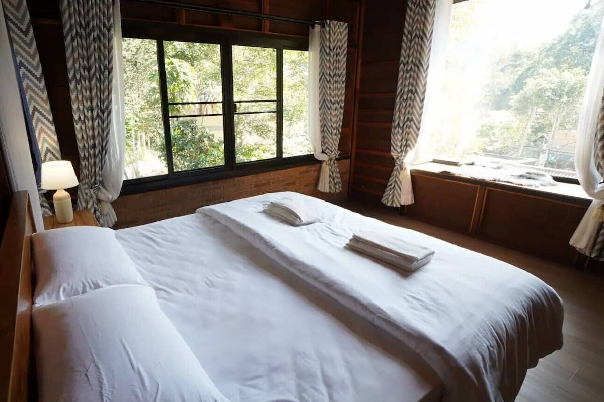 A hotel room with a large bed, a nightstand with a lamp, and a window with curtains.