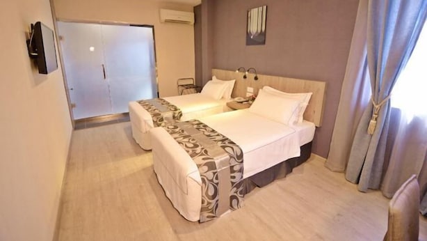 A hotel room with two beds, a TV, a painting on the wall, and a door leading to a bathroom. - Diamond Inn (Kota Kinabalu)