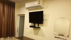 Een hotelkamer met een houten tafel, een flatscreen televisie aan de muur, een airconditioningsysteem boven de televisie, een spiegel en een deur met een handgreep.