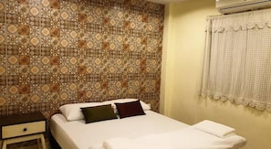 Una habitación de hotel con pared estampada, cama con almohadas, mesita de noche y ventana con cortina.