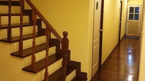 A hallway with a wooden staircase and a door at the end. - Papermoon (Bangkok)