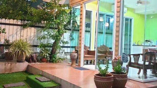 Een modern interieur met een glazen deur naar een lichte ruimte, een klein buitenstuk met kunstgras en potplanten, en een houten plafond.