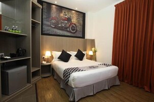 Habitación de hotel con cama, mesitas de noche, armario, un escritorio pequeño y un póster de motocicleta en la pared.