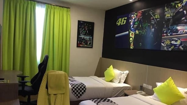 A hotel room with two beds, a desk, a yellow gaming chair, and a large TV displaying a racing game. - Swiss-belexpress Nilai (Nilai)