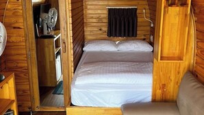 Interior acogedor de una cabaña de madera, con una cama, un pequeño rincón de descanso y una puerta que da a un kitchenette.