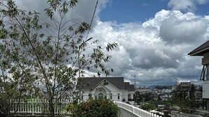Un barrio residencial con valla blanca, un jardín con flores rojas y una casa al fondo.