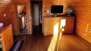 Un interior acogedor de madera con techo curvo, una pequeña kitchenette y un rincón de estar con vistas al exterior.