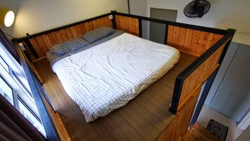 Un dormitorio con una cama litera de madera, una colcha blanca acolchada y un ventilador negro en la pared.