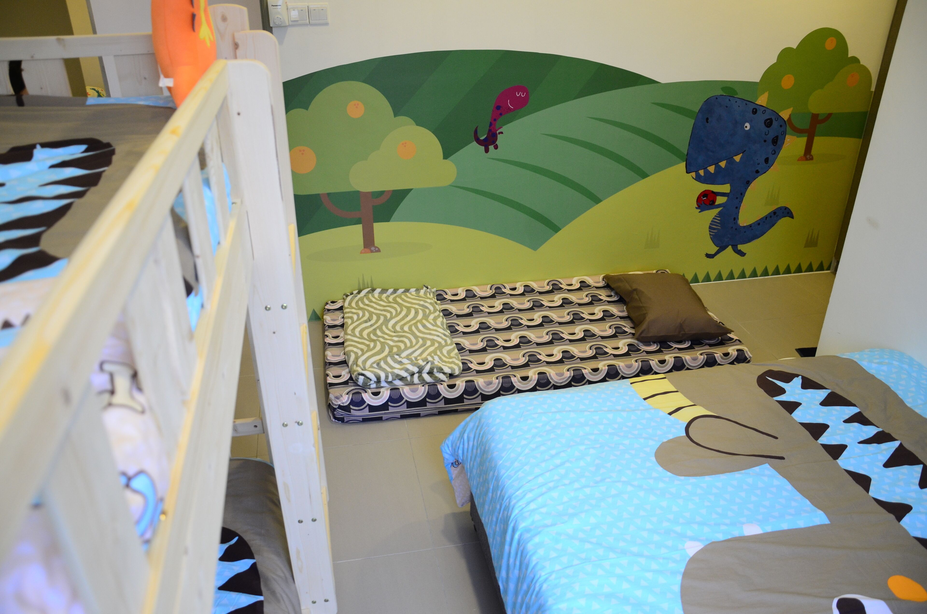 A children's bunk bed with a mural of a dinosaur and trees on the wall behind it.