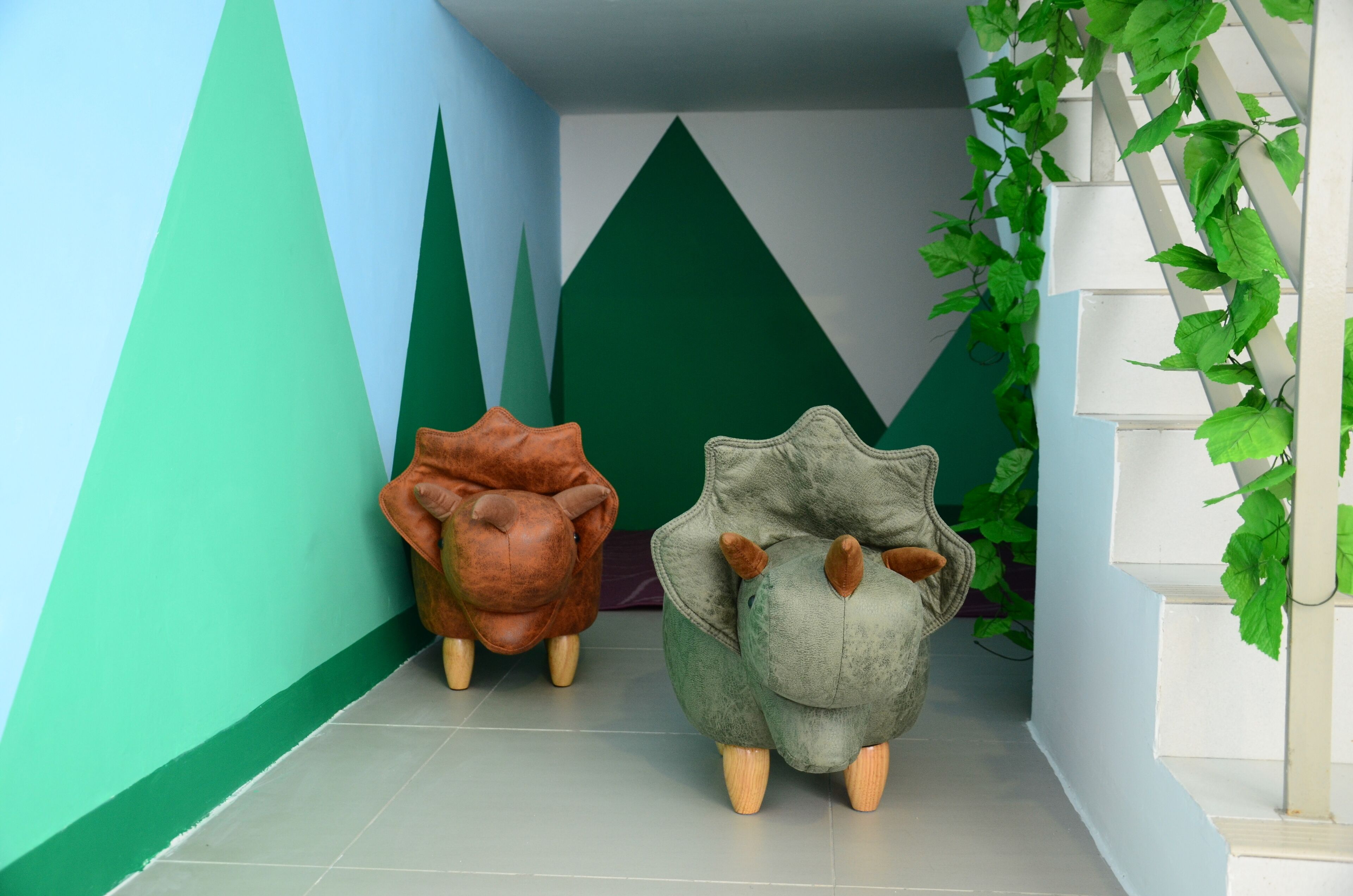 Two animal-shaped chairs in a hallway with geometric wall designs and a plant on a white trellis.