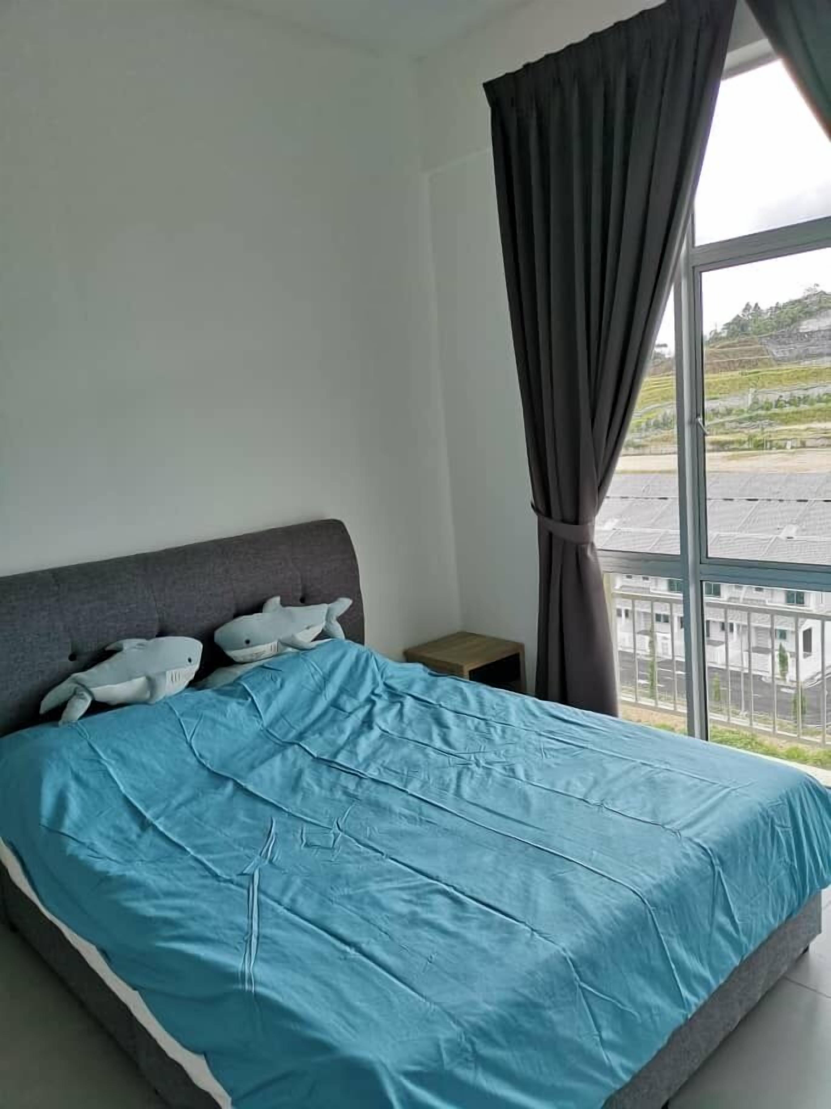 A bedroom with a bed, a nightstand, a window with curtains, and a view of a parking lot and buildings.