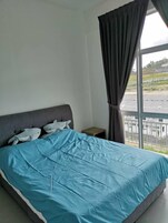 Une chambre à coucher avec un lit, une table de chevet, une fenêtre avec des rideaux et une vue sur un parking et des immeubles.