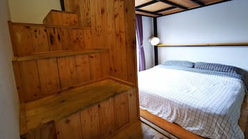 Una escalera de madera que lleva a una cama con cabecera y una ventana con cortinas.