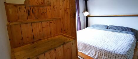 Uma escada de madeira leva a uma cama com cabeceira e janela com cortinas.