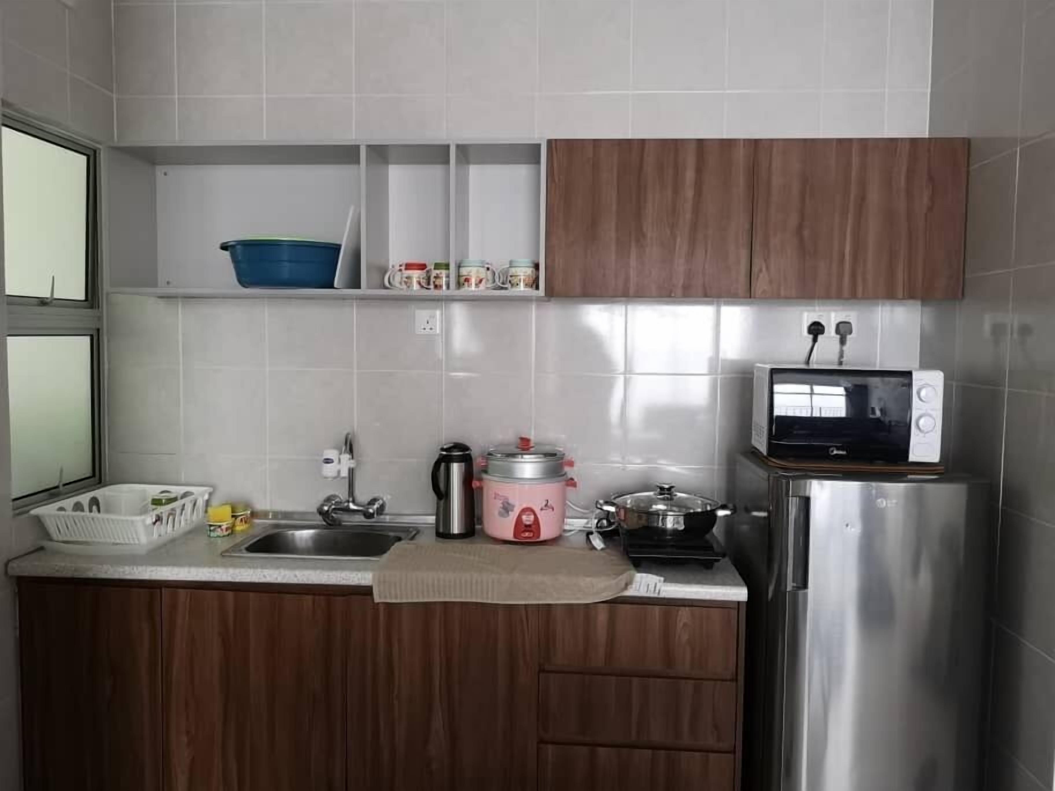 A kitchen with wooden cabinets, a stainless steel refrigerator, a microwave, a sink, and a countertop with various kitchen items.