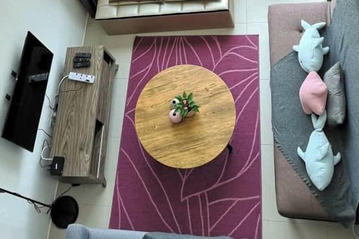 A modern living room with a round wooden coffee table, a sofa with shark-shaped pillows, and a large purple rug.