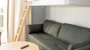 Un lit superposé avec un matelas, un canapé, une petite table ronde et une fenêtre avec des rideaux.